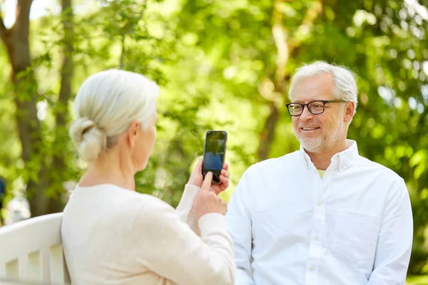 Old woman photographing man by smartphone in park — Stock Photo, Image