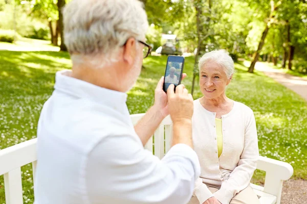 Старик фотографирует женщину на смартфон в парке — стоковое фото