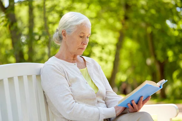 Счастливая пожилая женщина читает книгу в летнем парке — стоковое фото