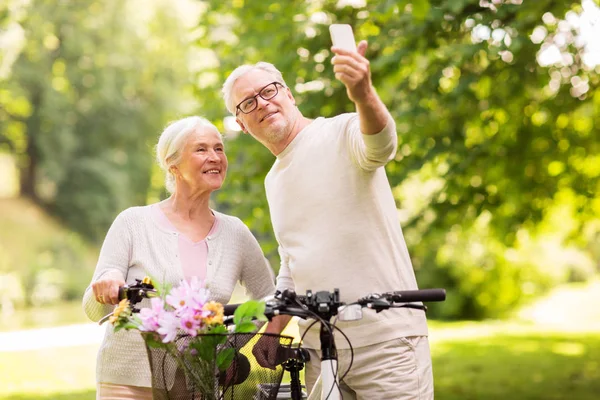 Couple aîné avec vélos prenant selfie au parc — Photo