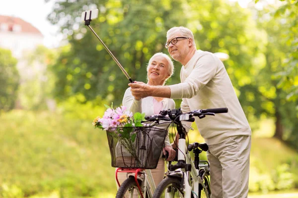 Para seniorów z rowerami robiącymi selfie w parku — Zdjęcie stockowe