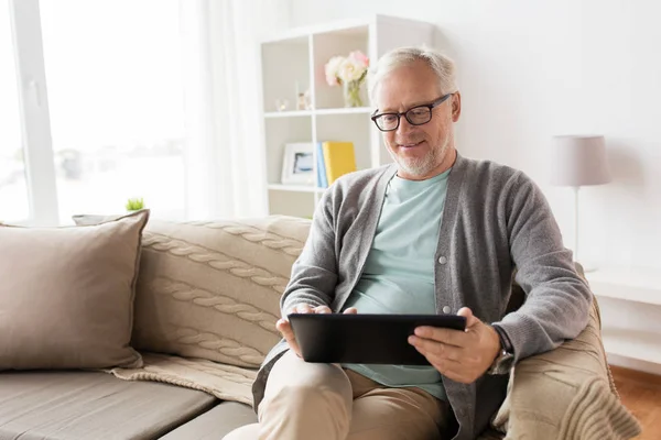 Starszy człowiek z komputera typu tablet, siedząc na kanapie w domu — Zdjęcie stockowe