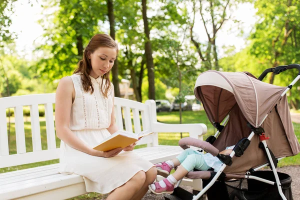 Мать с ребенком в коляске читает книгу в парке — стоковое фото