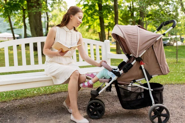 Mother with child in stroller reading book at park — Stock Photo, Image
