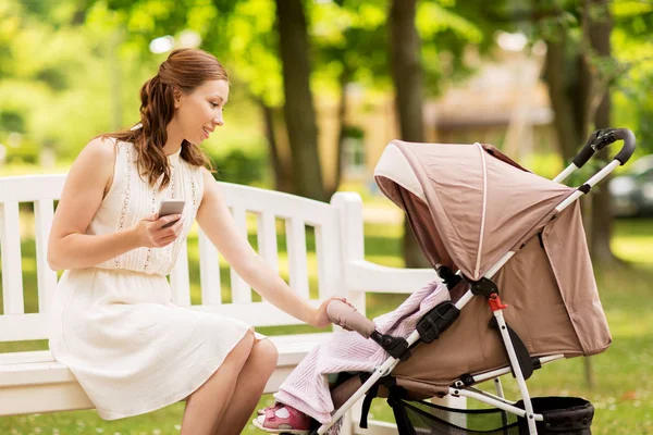 Счастливая мама со смартфоном и коляской в парке — стоковое фото