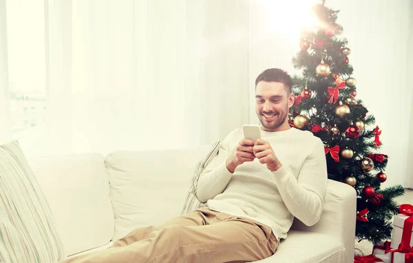 Hombre sonriente con teléfono inteligente en casa para Navidad —  Fotos de Stock