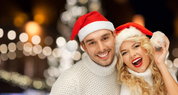 幸福的夫妇，在圣诞老人的帽子在圣诞灯 — 图库照片