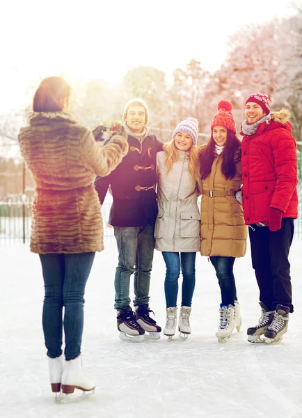 Amigos felices con smartphone en pista de patinaje sobre hielo —  Fotos de Stock