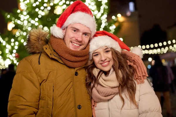 Coppia felice in cappelli di Babbo Natale all'albero di Natale — Foto Stock