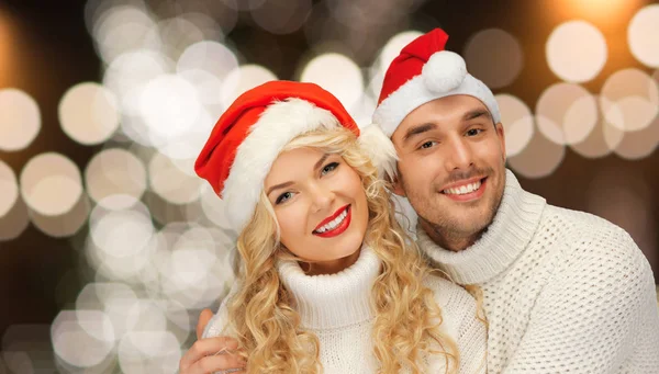 Glückliches Paar in Weihnachtsmützen über der Weihnachtsbeleuchtung — Stockfoto