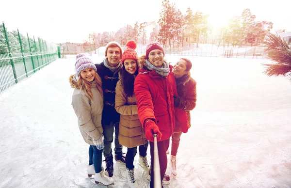 Amigos felizes com smartphone na pista de patinação no gelo — Fotografia de Stock