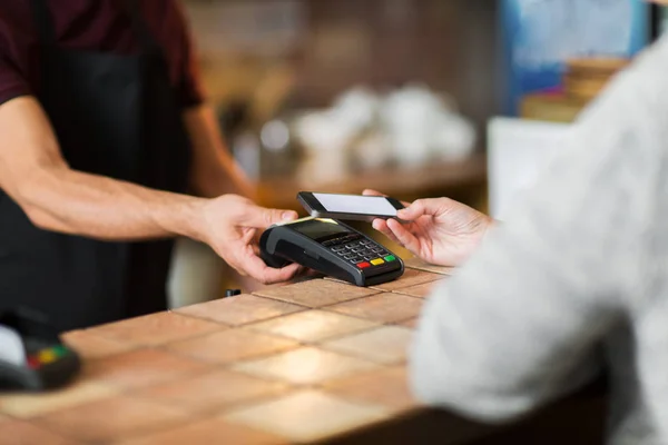 Hands with payment terminal and smartphone at bar — Stock Photo, Image