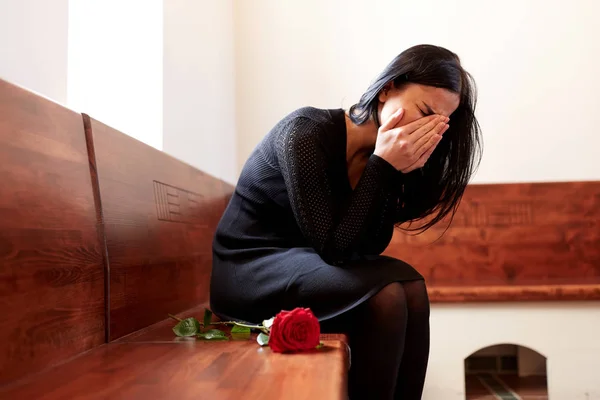 Weinende Frau mit roter Rose bei Beerdigung in Kirche — Stockfoto