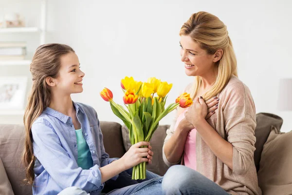 Menina feliz dando flores para a mãe em casa — Fotografia de Stock