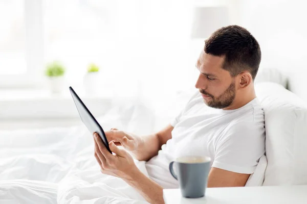 Jeune homme avec tablette PC dans le lit à la maison chambre — Photo
