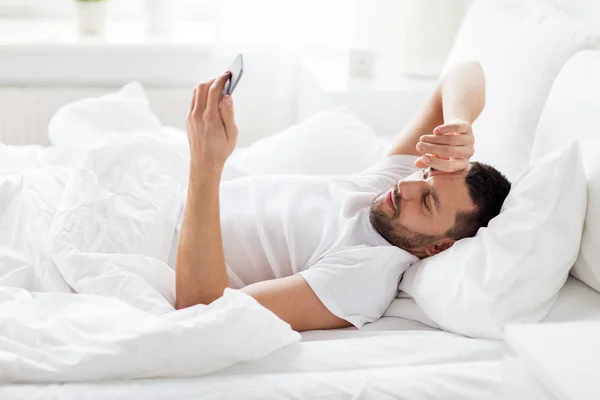 Jovem com smartphone na cama de manhã — Fotografia de Stock