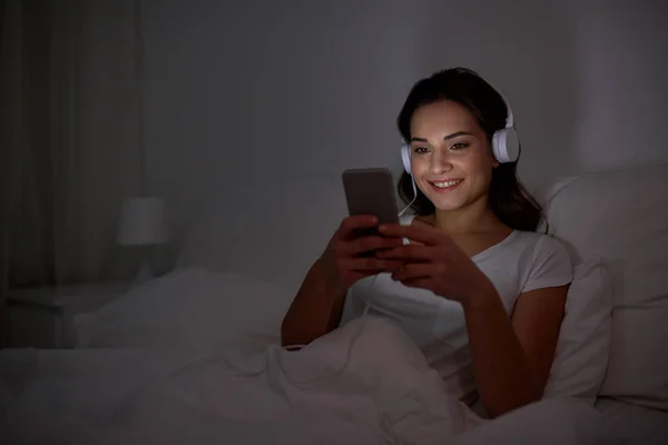 Женщина со смартфоном и наушниками в постели — стоковое фото