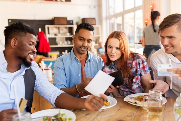 Gelukkige vrienden met geld betalen bij restaurant — Stockfoto