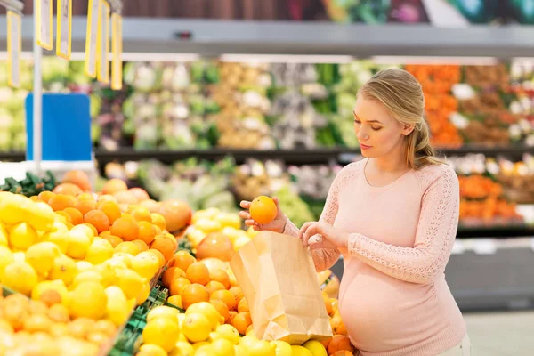 Mujer embarazada con bolsa de comprar naranjas en la tienda de comestibles — Foto de Stock