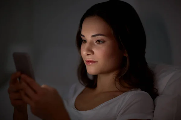 Feliz joven con teléfono inteligente en la cama por la noche —  Fotos de Stock