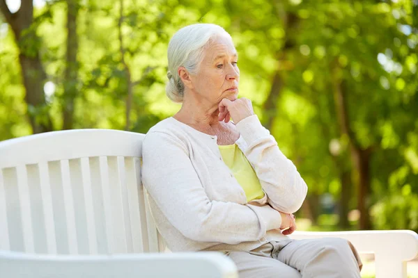 Сумна старша жінка сидить на лавці в літньому парку — стокове фото