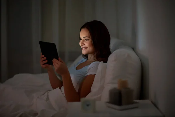 Mujer joven con tableta pc en la cama en el dormitorio en casa —  Fotos de Stock
