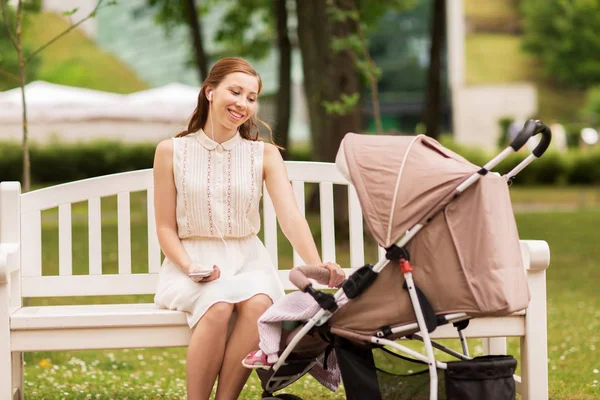 Счастливая мама со смартфоном и коляской в парке — стоковое фото