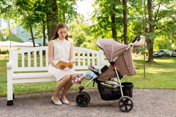 Mutter mit Kind im Kinderwagen liest Buch im Park — Stockfoto