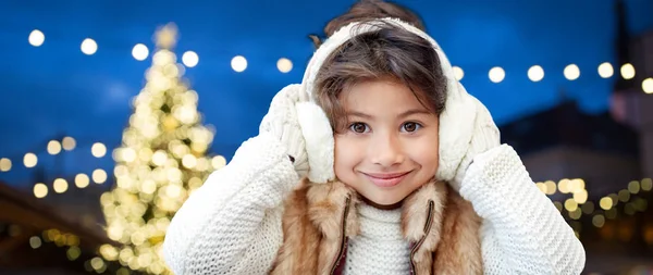 Happy girl wearing earmuffs over christmas lights — Stock Photo, Image