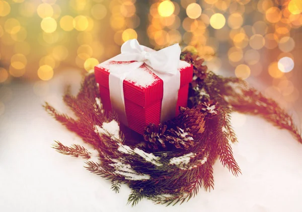 Рождественский подарок и еловый венок с шишками на снегу — стоковое фото