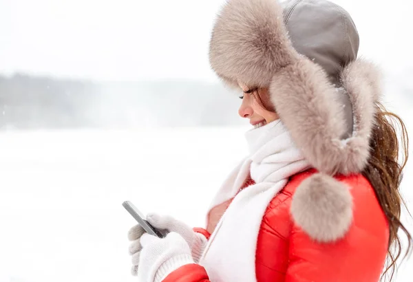 Šťastná žena v Zimní kožešinové čepice s smartphone — Stock fotografie