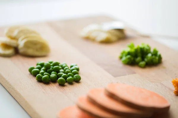 Ärter och andra grönsaker på träskiva — Stockfoto