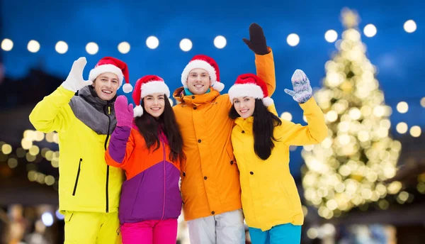 Přátelé v santa klobouky a lyžařské komplety na Vánoce — Stock fotografie