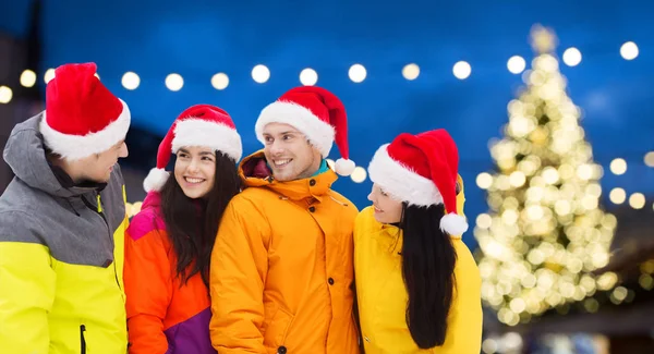 Přátelé v santa klobouky a lyžařské komplety na Vánoce — Stock fotografie
