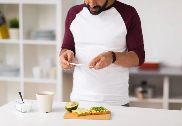 Hombre fotografiando comida por teléfono inteligente en casa —  Fotos de Stock