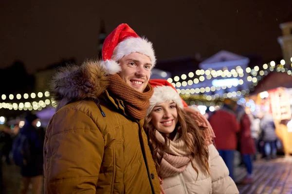 Heureux couple dans chapeaux de Père Noël au marché de Noël — Photo