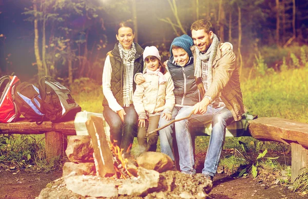 Familia feliz sentado en el banco en el fuego del campamento — Foto de Stock