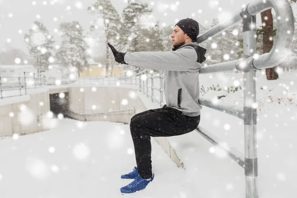 Спортивный человек делает приседания на заборе в зимний период — стоковое фото