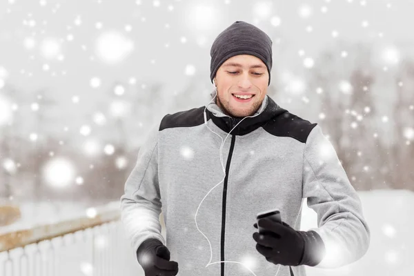 Счастливый человек с наушниками и смартфоном зимой — стоковое фото