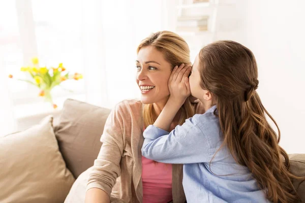Menina feliz sussurrando segredo para sua mãe em casa — Fotografia de Stock