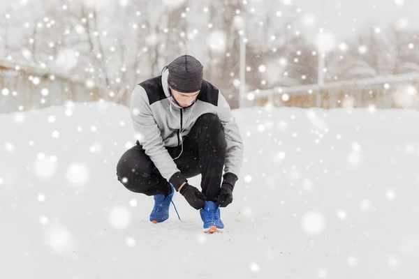 Человек в наушниках завязывает спортивную обувь зимой — стоковое фото
