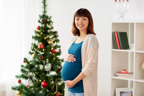 Счастливая беременная у новогодней елки дома — стоковое фото