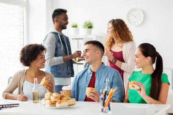 Счастливые друзья или команда едят на вечеринке в офисе — стоковое фото