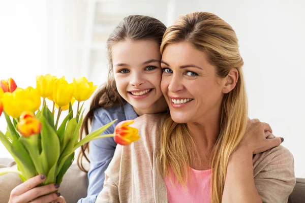 Menina feliz dando flores para a mãe em casa — Fotografia de Stock