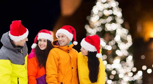 Friends in santa hats and ski suits at christmas — Stock Photo, Image