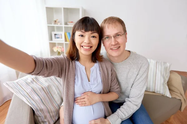 Gravid kvinna med man tar selfie hemma — Stockfoto