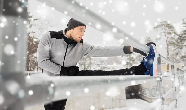 sports man stretching leg at fence in winter