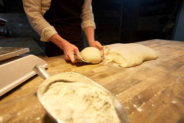 Baker portioning dough with bench cutter at bakery — Stock Photo, Image