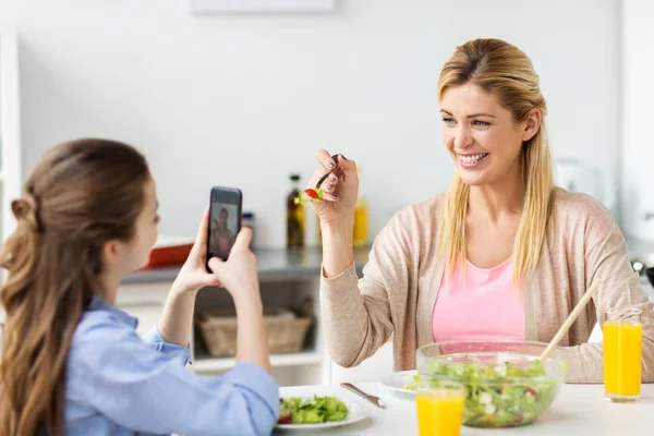 Chica fotografiando madre por teléfono inteligente en casa —  Fotos de Stock