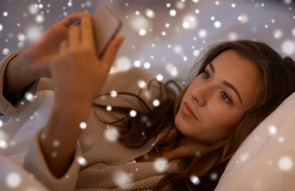 Молодая женщина со смартфоном в постели в спальне — стоковое фото